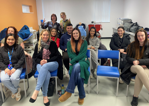 A group of trainees sat in chairs in a training room with manekins on the sides and the trainers stood at the back