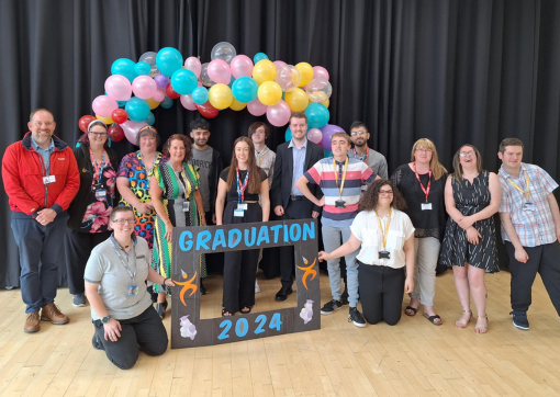 A photo of our the graduates with a balloon arch and a black selfie frame saying Graduation 2024